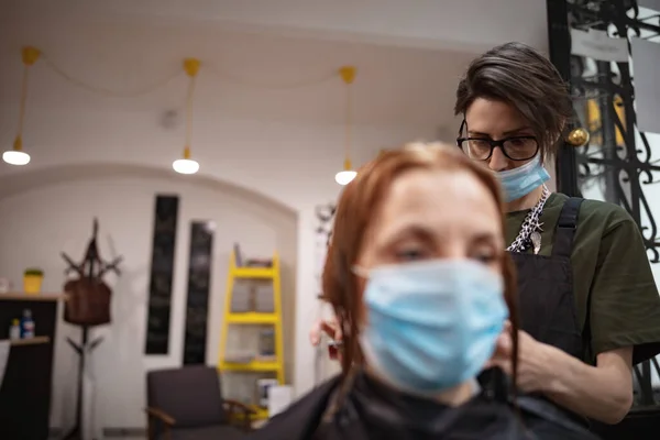 Hairdresser and customer in a salon with medical masks during virus pandemic. Working with safety mask.