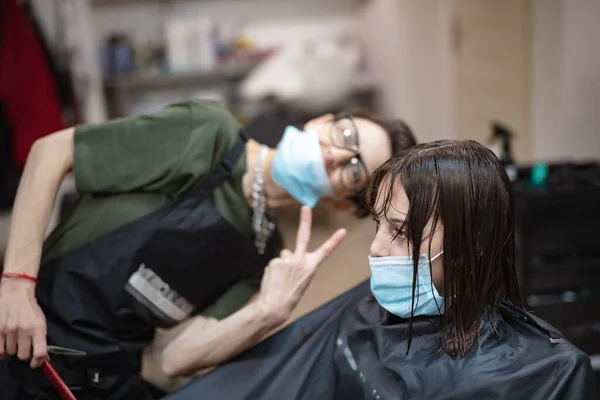 Hairdresser and girl child customer in a salon with medical masks during virus pandemic. Working with safety mask.