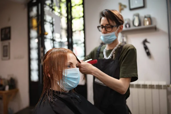 Hairdresser and customer in a salon with medical masks during virus pandemic. Working with safety mask.