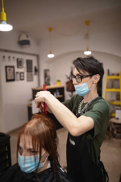 Hairdresser and customer in a salon with medical masks during virus pandemic. Working with safety mask.