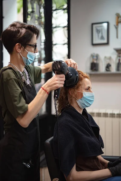 Hairdresser and customer in a salon with medical masks during virus pandemic. Working with safety mask.