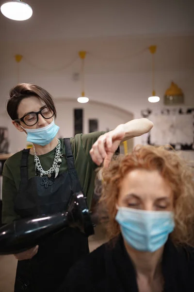 Hairdresser and customer in a salon with medical masks during virus pandemic. Working with safety mask.