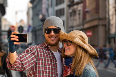 Şehir ortamında fotoğraf çekmek için akıllı telefon kullanan genç turist çifti.