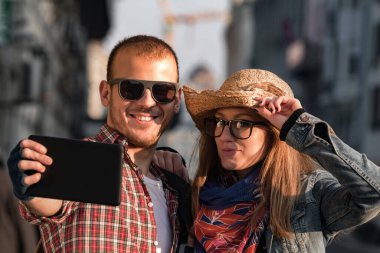 Şehir ortamında fotoğraf çekmek için akıllı tablet kullanan genç turist çifti.