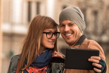Şehir ortamında fotoğraf çekmek için akıllı tablet kullanan genç turist çifti.