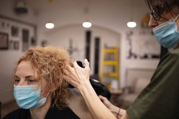 Hairdresser and customer in a salon with medical masks during virus pandemic. Working with safety mask.