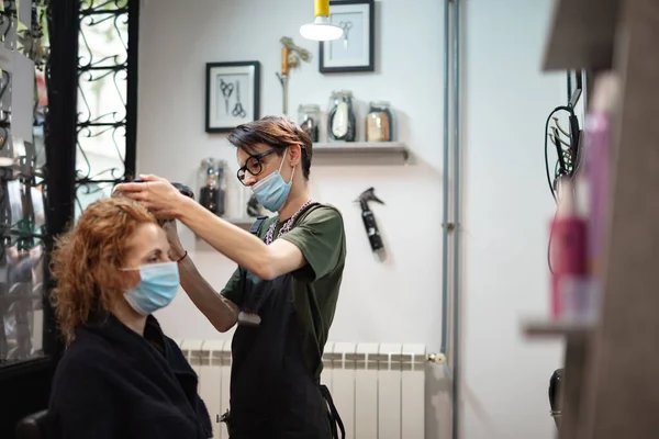Hairdresser and customer in a salon with medical masks during virus pandemic. Working with safety mask.