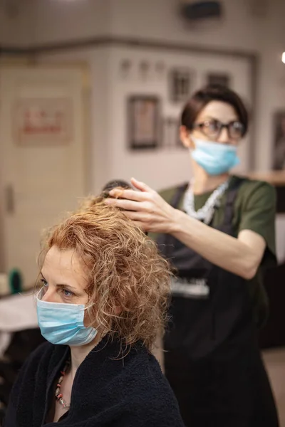 Hairdresser and customer in a salon with medical masks during virus pandemic. Working with safety mask.