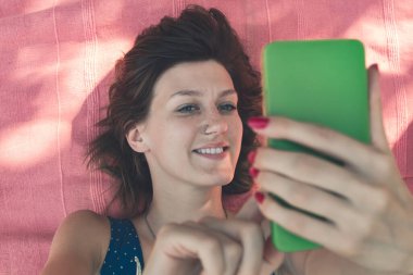 Doğada bir battaniyenin üzerinde uzanırken akıllı telefon kullanan genç bir kadın..