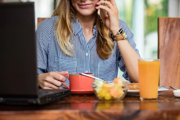 早餐时在家使用笔记本电脑和手机的妇女 自由职业概念 — 图库照片