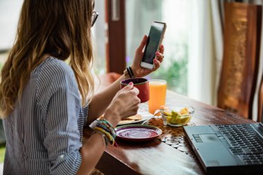 Kahvaltıda dizüstü bilgisayar ve cep telefonu kullanan bir kadın. Bağımsız çalışma kavramı..