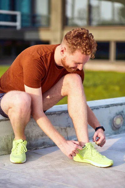 Young man tying running shoes and exercising / stretching in urban park.