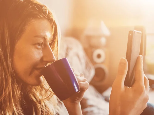 Woman using cellphone and drinking coffee alone at home - ordering food and groceries from home, over the phone during isolation.