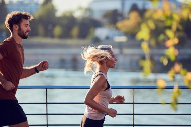 Nehir kenarındaki kentsel çevrede koşan / egzersiz yapan modern kadın ve erkek.