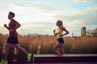 Nehir kenarındaki kentsel çevrede koşan / egzersiz yapan modern kadın ve erkek.