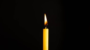 Siyah bir arkaplanda aydınlatılmış sarı bir mumun yakın çekimi.