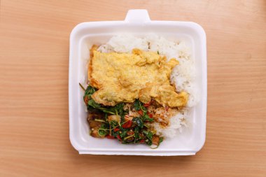 Yakın plan yiyeceklere çıtır domuz eti, fesleğen ve lezzetli omlet denir. Tahta masanın arkasındaki köpük kutuda..