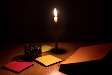 Masaya mumlardan gelen turuncu ışıkla dizilmiş not defterlerinin ve ataçların yakın plan fotoğrafları..