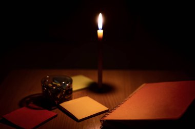 Masaya mumlardan gelen turuncu ışıkla dizilmiş not defterlerinin ve ataçların yakın plan fotoğrafları..