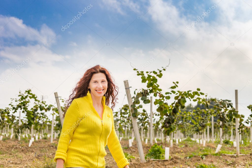 Yellow dressed menopausal woman enjoying nature of a countryside while walking in the kiwi orchard in Autumn season