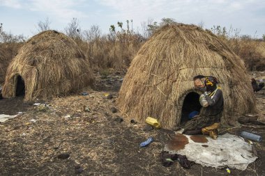 Omorate Ethiopia - January 24: Unidentified woman of the Mursi tribe drinking in a bowl next to her house in a traditional village of the Mursi on January 24, 2018 in Omo valley, Ethiopia. clipart