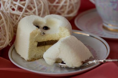 Beyaz kadife kremalı pasta bir fincan tabağının üzerinde yatar ve çay kaşığının bir parçasını koparırlar.