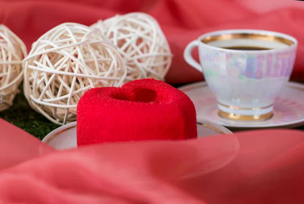 red velvet mousse cake with a cup of tea or coffee on a background of clouds of pink fabric and rattan balls closeup