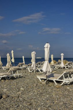 Mavi gökyüzüne karşı güneşli yataklı ve şemsiyeli çakıl taşı plajı