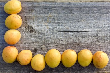 Pembe varili olan parlak, sarı kayısılar eski bir ahşap arka planda yatıyor ve metin için bir çerçeve oluşturuyor.