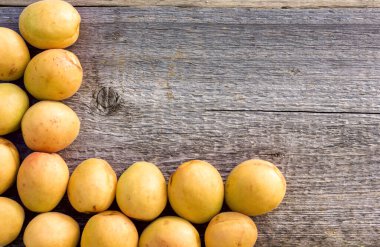 Pembe varili olan parlak, sarı kayısılar eski bir ahşap arka planda yatıyor ve metin için bir çerçeve oluşturuyor.