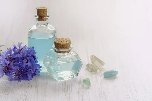 Cornflower flower and blue water or aromatherapy oil in glass bottle. Natural mineral crystals on white wooden table background, copy space