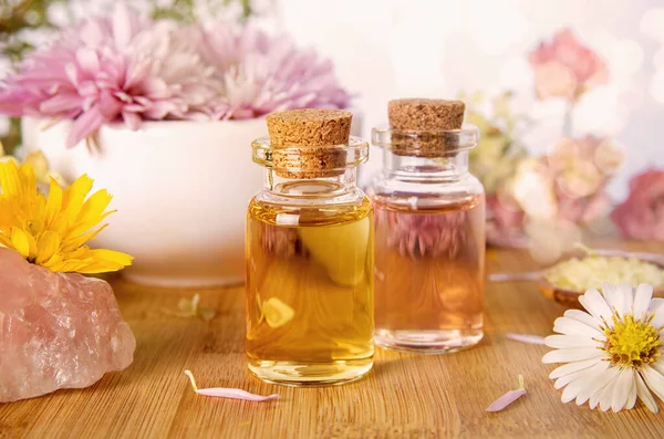 Essential herbal oil for aromatherapy, rose quartz crystals and chrysanthemum flowers on wooden background