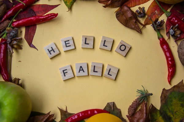 Text spelt with wooden letter tiles on pale yellow background, words HELLO FALL, autumn still life, lettering concept