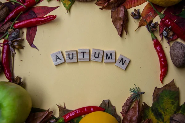 Text spelt with wooden letter tiles on pale yellow background, word AUTUMN, autumn still life, lettering concept