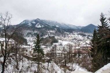 Dağlarda kış, güzel karla kaplı evler, karlı ağaçlar ve bulutlu sisli beyaz gökyüzü.