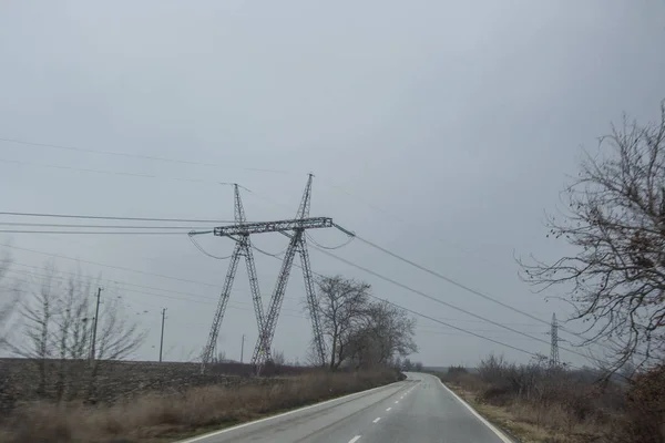 Misty car road in Bulgaria with electricity pylons with wires, wintertime fog on the road