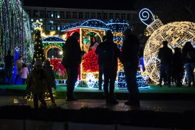 Varna, Bulgaristan - 7 Aralık 2019 - Renkli Noel süslemeleri ve geceleri ışıklar, yeni yıl tatili dekorasyonu, Varna şehir meydanı, insanların silüetleri