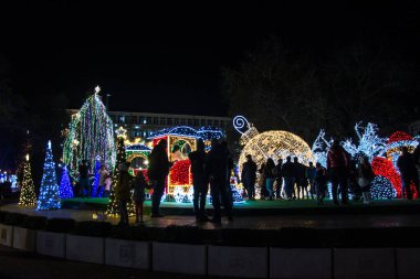 Varna, Bulgaristan - 7 Aralık 2019 - Renkli Noel süslemeleri ve geceleri ışıklar, yeni yıl tatili dekorasyonu, Varna şehir meydanı, insanların silüetleri