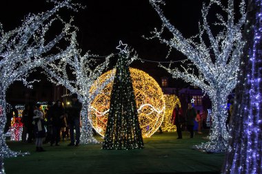 Varna, Bulgaristan - 7 Aralık 2019 - Renkli Noel süslemeleri ve geceleri ışıklar, yeni yıl tatili dekorasyonu, Varna şehir meydanı, insanların silüetleri