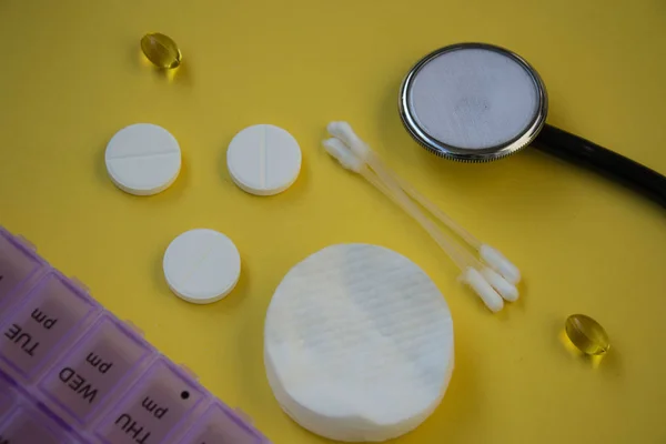 Bunch of pills and capsules, box for storage of drugs and medical stethoscope and blood pressure meter on yellow background, healthcare concept