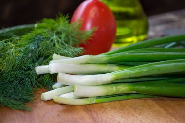 Taze taze soğanlar, yeşil otlu dereotu ve domates mutfakta ahşap masada, pişirmeye hazır.
