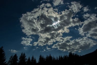 Güzel bulutlar mavi gökyüzüne ve dağların ve ağaçların siluetlerine karşı, gündüz vakti ormanda