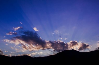 Mavi gökyüzüne karşı güzel bulutlar ve dağ ve ağaçların siluetleri, ormanda gündüz vakti, doğada gün batımı