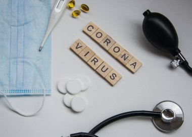 Beyaz arka planda CORONA VIRUS harfli ahşap fayanslar, covid-19, taç virüsü, termometre ve maske, sağlık steteskobu ve kan basıncı ölçer