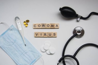 Beyaz arka planda CORONA VIRUS harfli ahşap fayanslar, covid-19, taç virüsü, termometre ve maske, sağlık steteskobu ve tansiyon ölçer, haplar