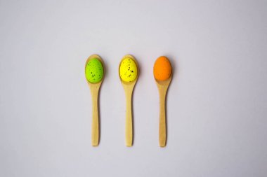 Soluk pembe arka planda renkli Paskalya yumurtaları, tahta kaşıklarda yumurta, yeşil, turuncu, sarı, yumurta avı dekorasyonu, düz bir düzen.