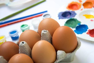 Kutuda paskalya yumurtası, bulanık boyalar, arka planda renkli paletler, beyaz arka planda boya ekipmanları.