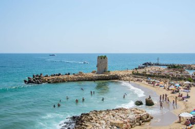 Deniz manzarası, insanlarla dolu bir sahil manzarası, eski bir kale kulesi ve kayalar ve tetrapodlar, mavi su ve gökyüzü, yaz mevsimi, doğa,