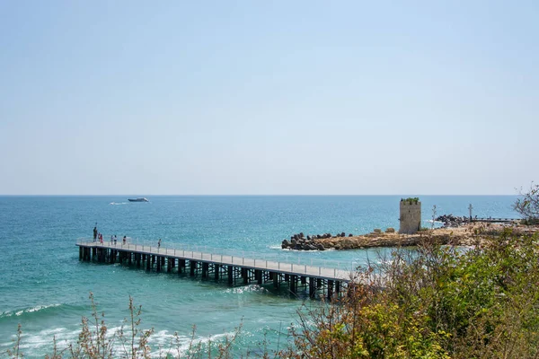 ポセイドン像のある桟橋を歩く人々 ビーチ 青い海と空の近くの橋 — ストック写真