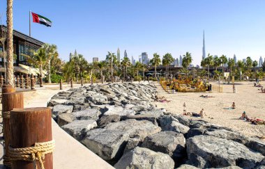 Dubai / UAE - December 20, 2019: La Mer Beach in Dubai. New modern public urban beach with beautiful city background. La Mer walk wuth UAE flag